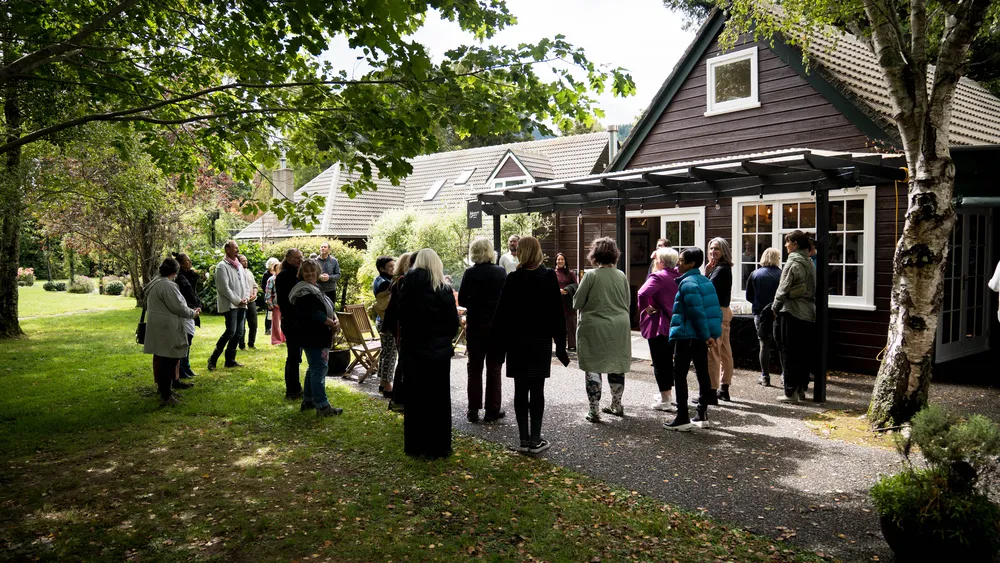 A group gathering in dappled light outside the lodge at Mangaroa Farms, trees overhead