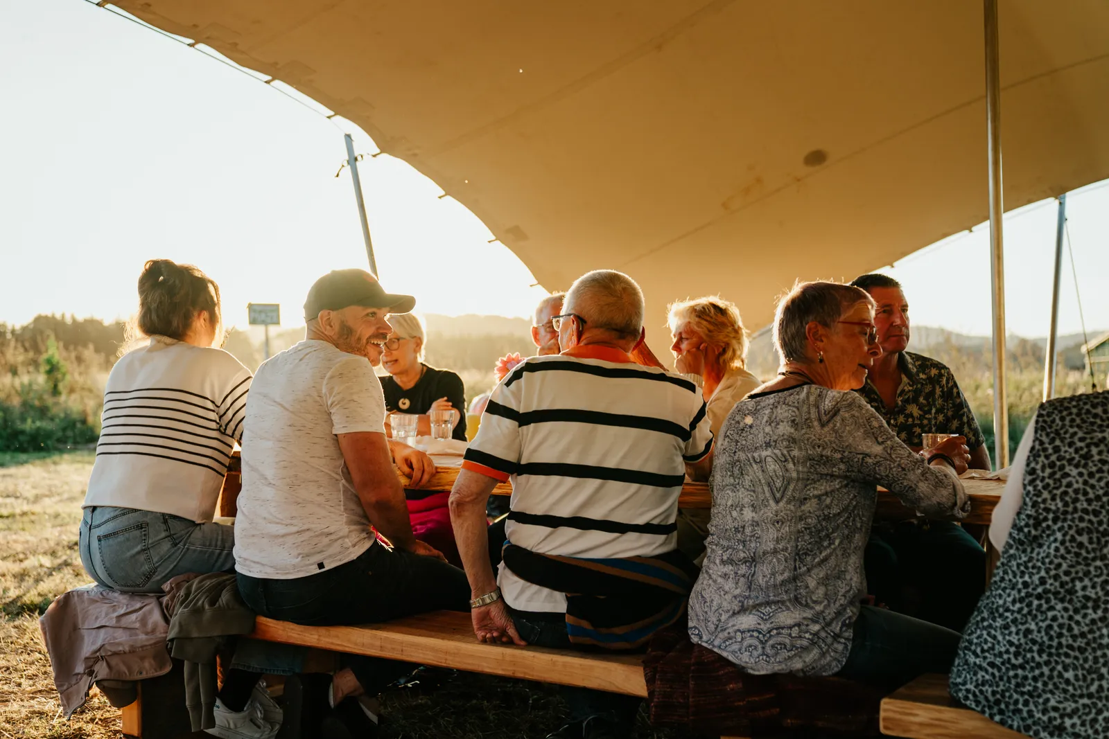 A long table of guests sharing a meal outdoors as the sun sets over the farm